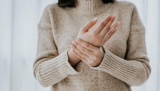 Frau mit Wollpullover, hält mit einer Hand ihre andere Hand fest.