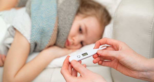 Kind, liegt auf der Couch, Mutter sitzt mit einem Fieberthermometer daneben.