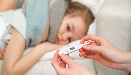 Kind, liegt auf der Couch, Mutter sitzt mit einem Fieberthermometer daneben.