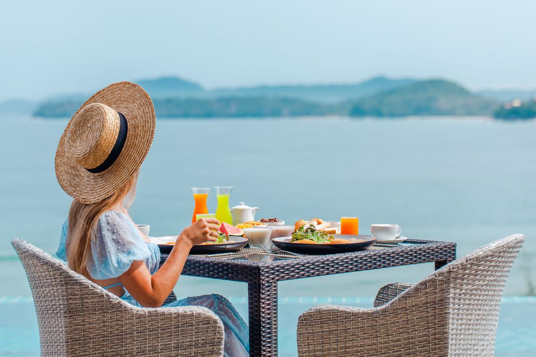 Junge Frau, sitzt an einem Esstisch mit Blick aufs Meer.
