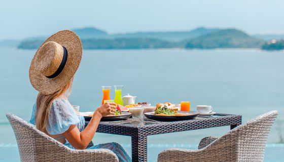 Junge Frau, sitzt an einem Esstisch mit Blick aufs Meer.