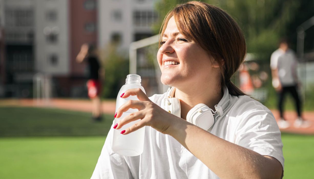 Übergewichtige Frau, trinkt aus einer Wasserflasche.