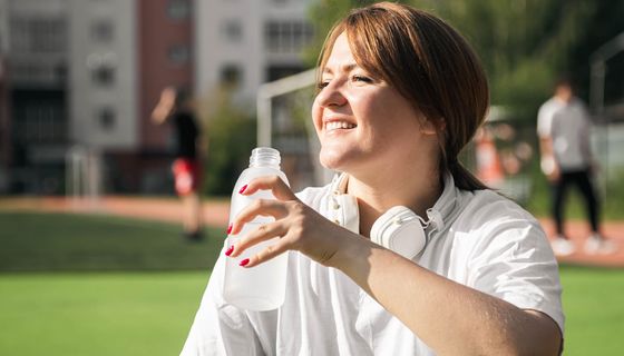 Übergewichtige Frau, trinkt aus einer Wasserflasche.