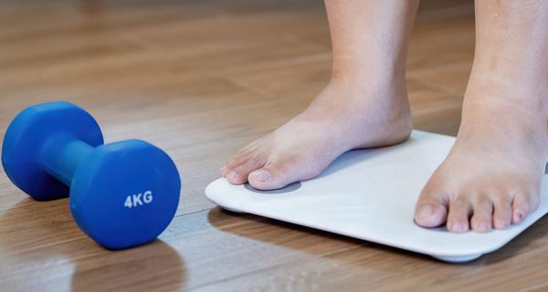 Zu sehen sind nur die Füßer einer Frau auf einer Waage, daneben eine 4kg-Hantel.