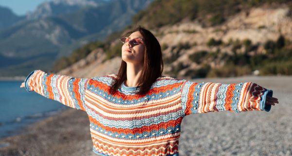 Junge Frau im bunten Pulli badet am Strand in der Sonne.
