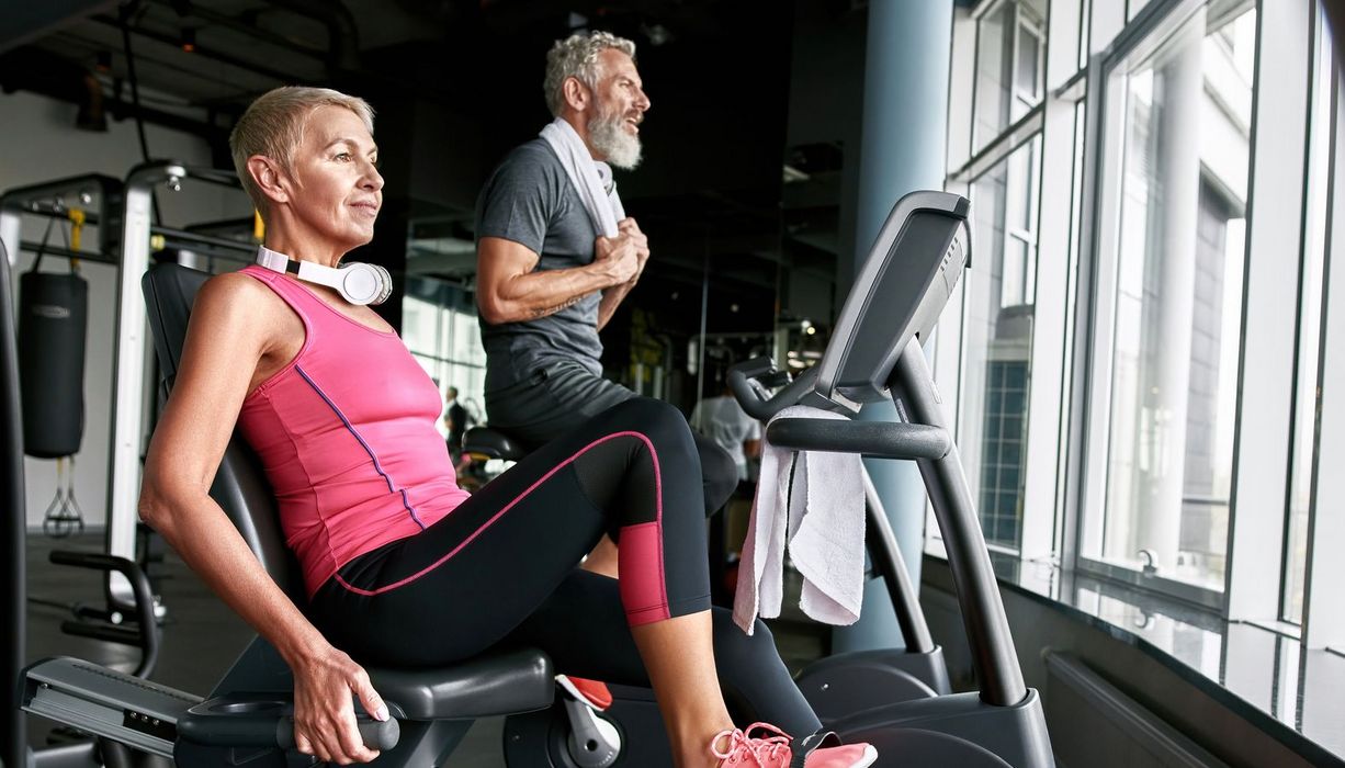 Eine Frau und ein Mann, beide über 65, trainieren in einem Fitnesstudio.