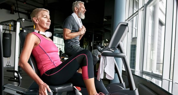 Eine Frau und ein Mann, beide über 65, trainieren in einem Fitnesstudio.