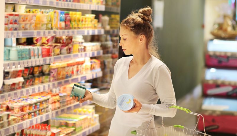 Eine junge Frau steht vor einem Supermarktregal und liest die Zutatenliste von einem Produkt.