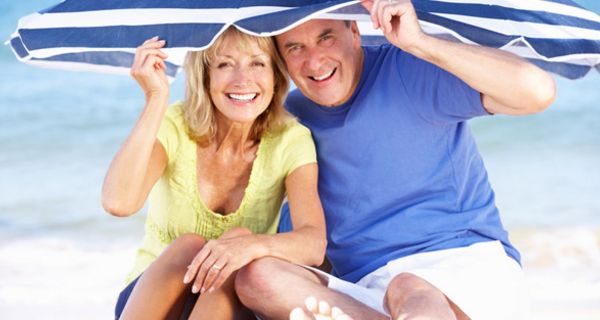 Ein Paar, ca, 60 Jahre alt, sitzt am Strand unter einem Sonnenschirm.