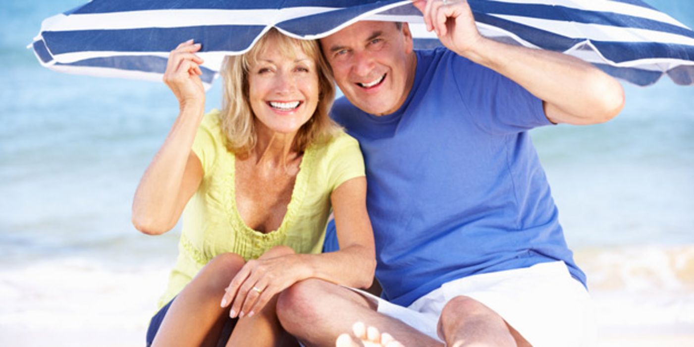 Ein Paar, ca, 60 Jahre alt, sitzt am Strand unter einem Sonnenschirm.