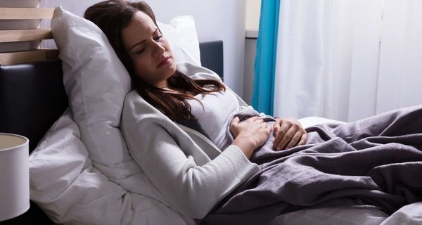 Junge Frau liegt mit Magenschmerzen im Bett.