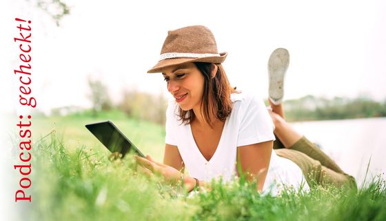 Junge Frau, liegt mit einem Tablet auf der Wiese und liest.