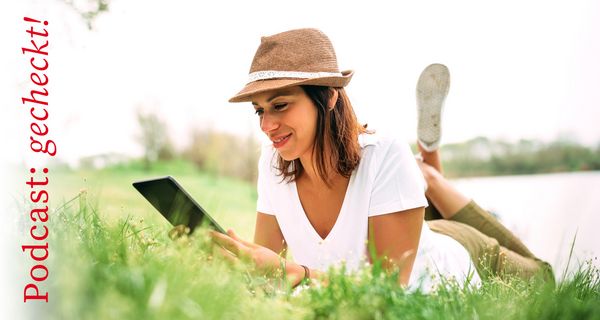 Junge Frau, liegt mit einem Tablet auf der Wiese und liest.