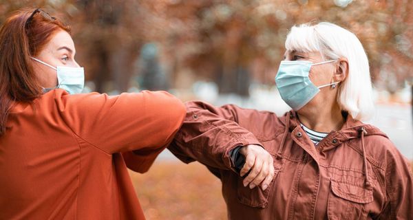 Zwei Frauen mit Maske, begrüßen sich durch ihre Ellenbogen.