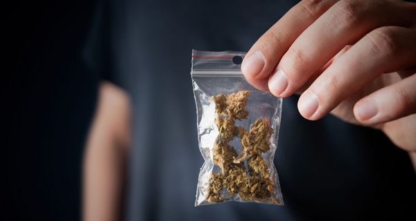 Mann, hält ein Päckchen Cannabis in die Kamera.