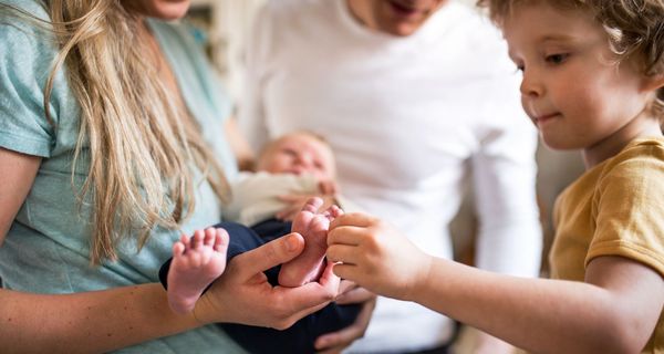 Junge Familie, Mutter hält Neugeborenes im Arm, kleiner Bruder staunt.