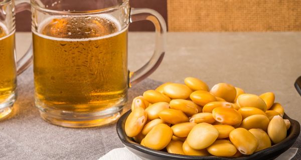 Schale mit gesalzenen Lupinen-Samen neben zwei Gläsern mit Bier.