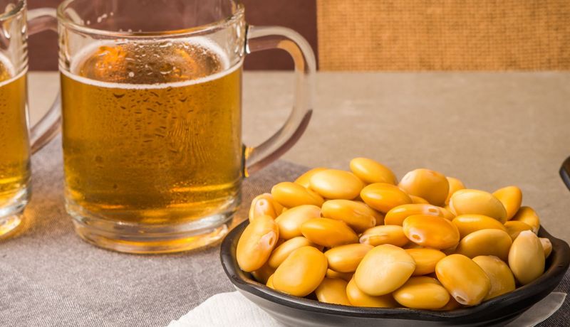 Schale mit gesalzenen Lupinen-Samen neben zwei Gläsern mit Bier.