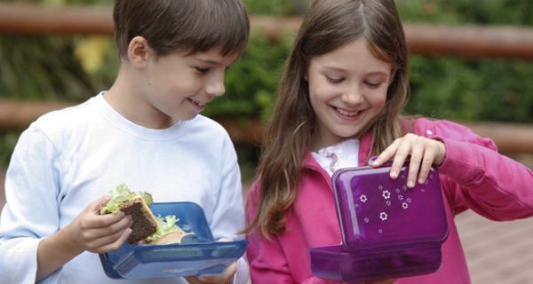 Junge und Mädchen mit Frühstücksbox auf dem Schulhof