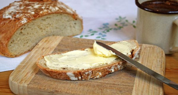 Butterbrot mit Messer auf einem Brett nebst Brotlaib und Kaffeetasse