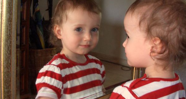 Kleines Mädchen schaut sich im Spiegel an.