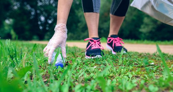 Frau mit Jogginghose, hebt leere Plastikflasche auf. 