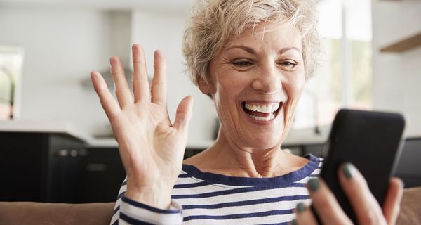 Ältere Frau, lacht in ihr Smartphone und winkt.