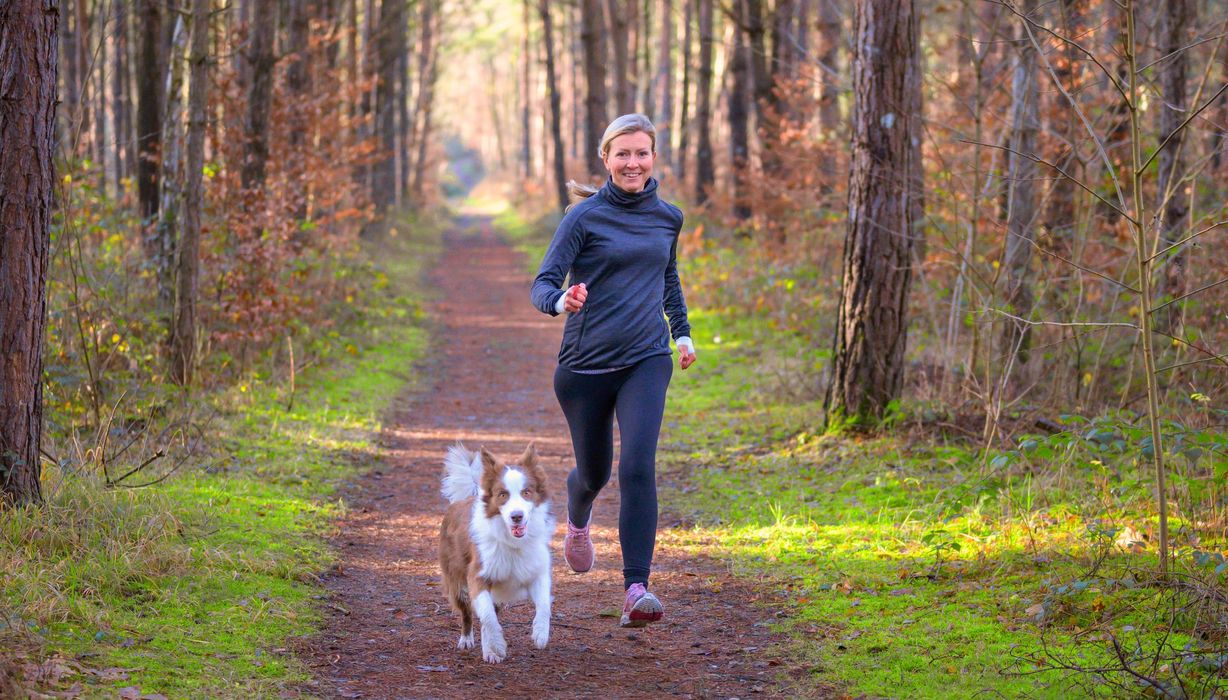 Frau joggt mit Hund am Morgen.