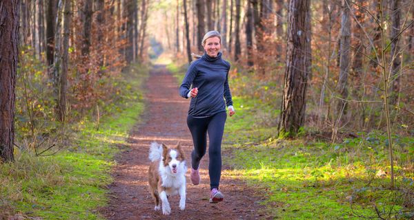 Frau joggt mit Hund am Morgen.