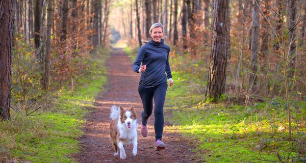 Frau joggt mit Hund am Morgen.