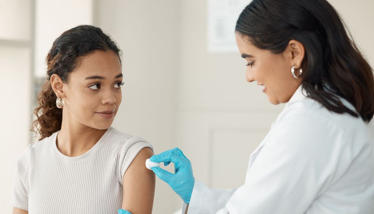 Eine Ärztin definiziert die Haut am Oberarm einer jungen Frau, um sie auf eine Impfung vorzubereiten.