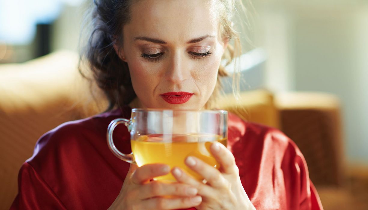 Frau blickt auf eine große Tasse grünen Tees in ihren Händen.