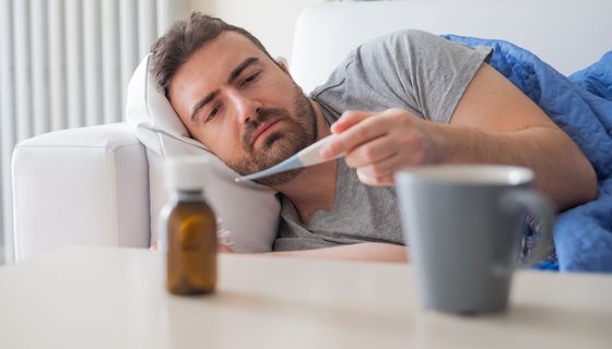 Erschöpfter Mann schaut auf Fieberthermometer.