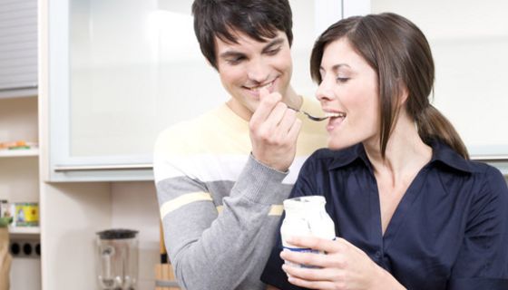Mann gibt Frau einen Löffel Joghurt.