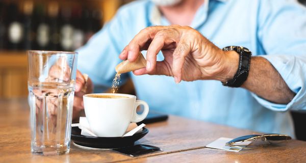 Mann streut sich Süßstoff in den Kaffee.