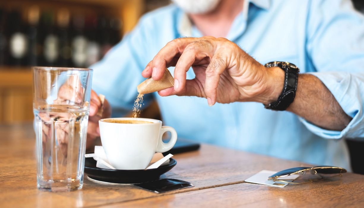 Mann streut sich Süßstoff in den Kaffee.