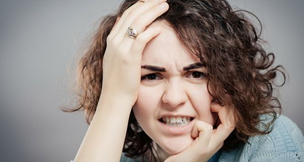 Nahaufnahme Gesicht, junge, dunkellockige Frau, linke Hand am Kinn, rechte an Schläfe, wutverzerrtes Gesicht, gerunzelte Stirn/Brauen