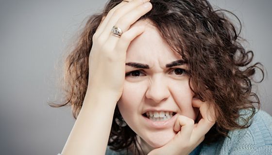 Nahaufnahme Gesicht, junge, dunkellockige Frau, linke Hand am Kinn, rechte an Schläfe, wutverzerrtes Gesicht, gerunzelte Stirn/Brauen