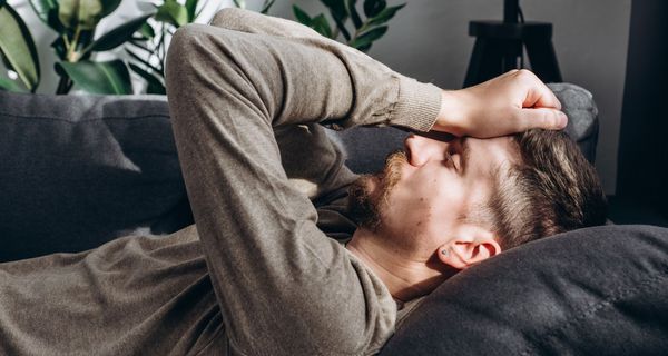 Junger Mann liegt mit geschlossenen Augen auf der Couch, die Daumenballen auf die Stirn gepresst. 
