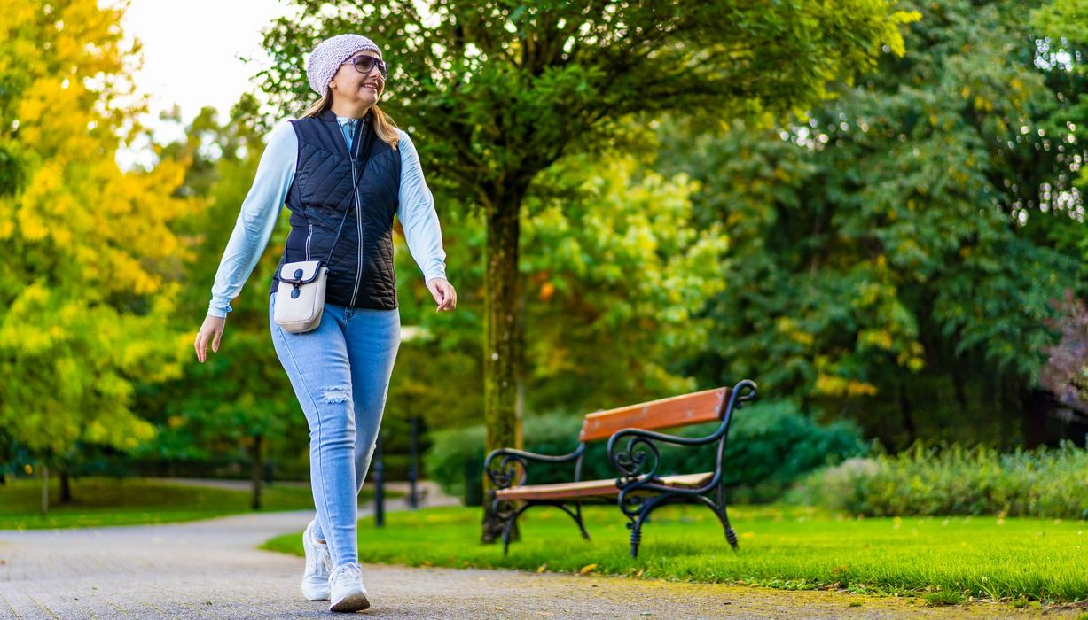 Frau, etwa 40 Jahre alt, geht in Alltagskleidung durch einen Stadtpark.