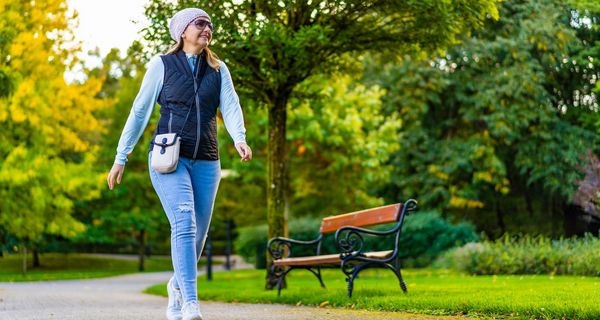 Frau, etwa 40 Jahre alt, geht in Alltagskleidung durch einen Stadtpark.