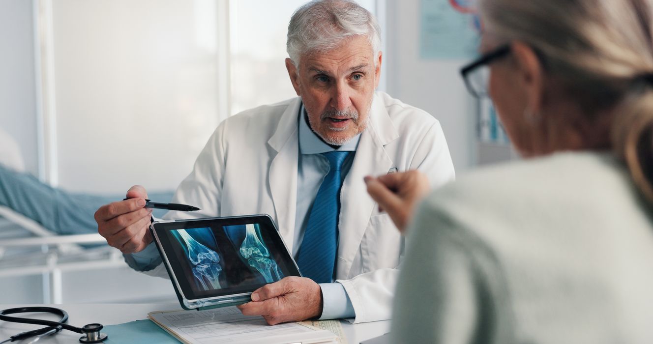 Ein Arzt zeigt einer Patientin Röntgenbilder der Knie auf einem Tablet.