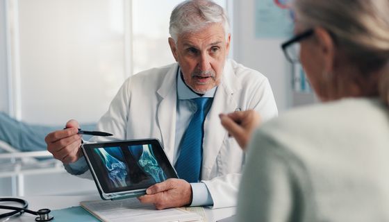 Ein Arzt zeigt einer Patientin Röntgenbilder der Knie auf einem Tablet.