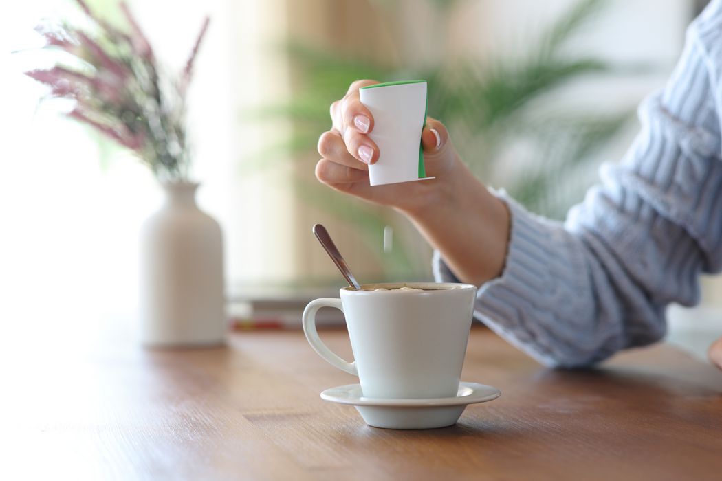 Eine Frau gibt eine Süßstofftablette aus einem Spender in eine Kaffeetasse.