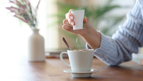 Eine Frau gibt eine Süßstofftablette aus einem Spender in eine Kaffeetasse.