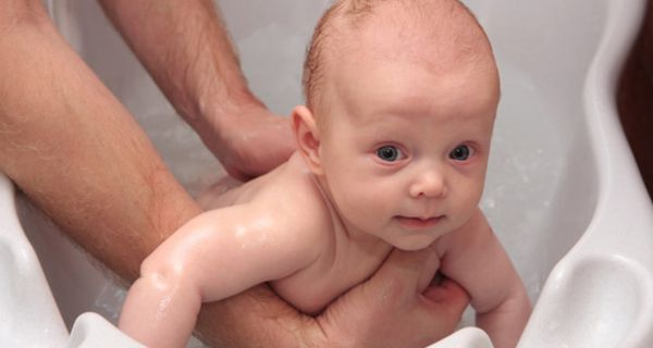 Erwachsener wäscht Baby in einer Wanne mit klarem Wasser