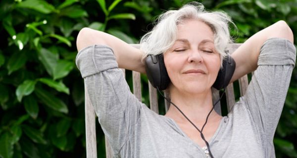 Vitale Seniorin sitzt im Freien und hört mit geschlossenen Augen Musik über einen Kopfhörer