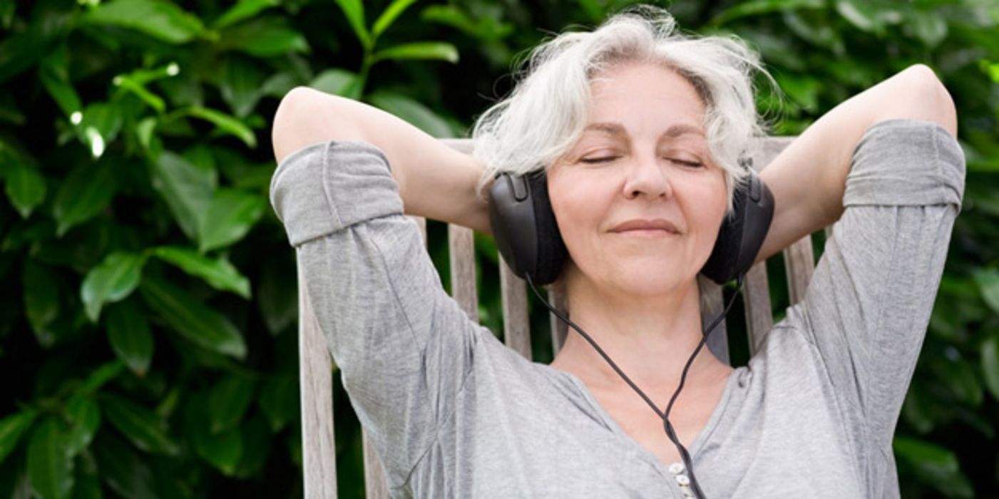 Vitale Seniorin sitzt im Freien und hört mit geschlossenen Augen Musik über einen Kopfhörer