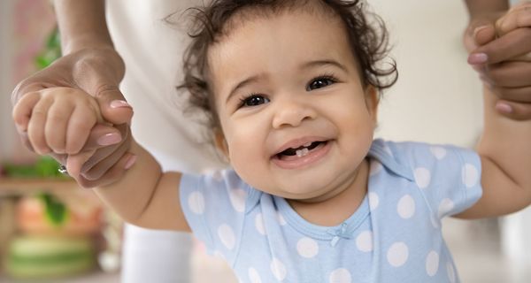 Baby, lächelt in die Kamera und zeigt die ersten Zähne.