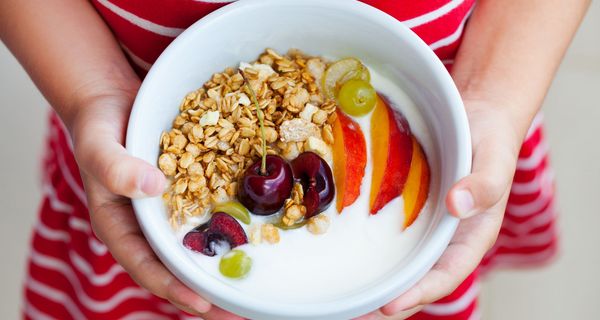 Frau im roten Kleid, hält eine Schale Joghurt mit Müsli und Obst in den Händen.